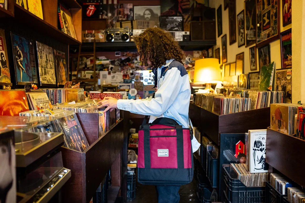 A person browsing vinyl in a record shop with a The Selektor record bag.